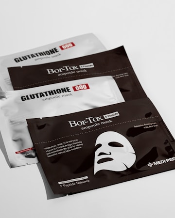 Three flat, rectangular packages are arranged on a white surface. Two of the packages are labeled 'GLUTATHIONE 600 ampoule mask' and are silver with black and red text. The middle package is labeled 'Bor-Tox ampoule mask' and is black with white text. The Bor-Tox package features a graphic of a facial mask and mentions skin elasticity and wrinkle care.