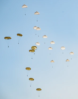 A group of veterans in uniform standing proudly with parachutes in the background under a clear blue sky.