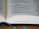 An open book laying on a wooden surface with visible text focusing on religious or biblical scripture. The book has a ribbon bookmark, and the pages display a mix of poetry-style verses and narrative text.