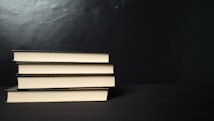 Four neatly stacked hardcover books with a black cover are placed horizontally against a dark background. The edges of the pages create a contrasting light color with the black covers.