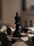A black king chess piece stands prominently on a wooden chessboard surrounded by fallen white and black pieces. The surface of the board displays intricate patterns, while the background is softly blurred, highlighting the central figure.