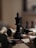 A black king chess piece stands prominently on a wooden chessboard surrounded by fallen white and black pieces. The surface of the board displays intricate patterns, while the background is softly blurred, highlighting the central figure.