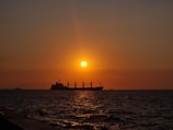A cargo ship sailing from Dubai’s port towards international waters at sunset.