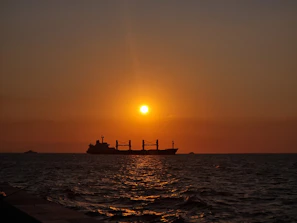 Container ship sailing across the ocean under a sunset sky.