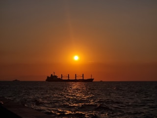 A cargo ship loaded with oil barrels sailing across the ocean at sunset