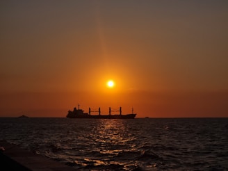 A modern cargo ship sailing across the ocean at sunset.