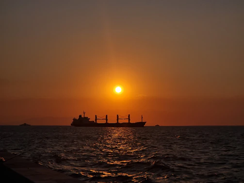 A cargo ship sailing at sunset, carrying goods across the ocean.