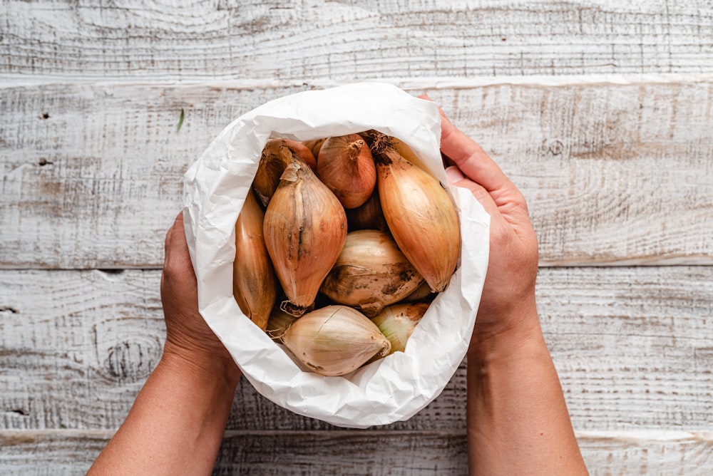 a person holding a paper bag filled with onions