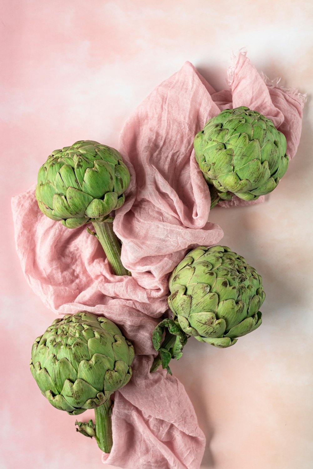 a bunch of green artichokes on a pink cloth