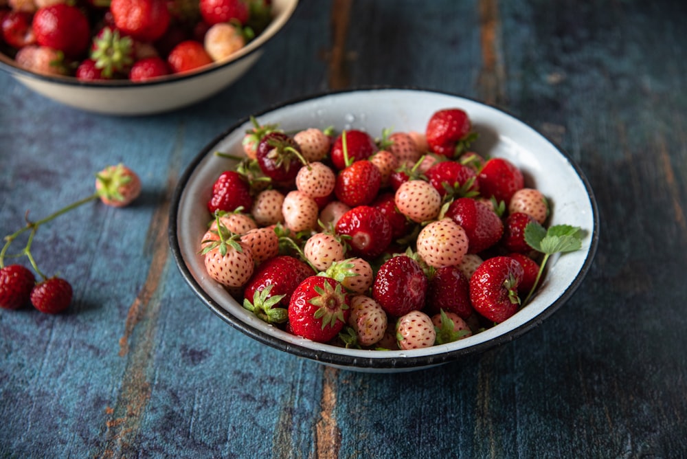 a bowl of strawberries on a table next to another bowl of strawberries