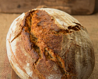 Close-up of a rustic sourdough loaf with a golden crust resting on a wooden board.