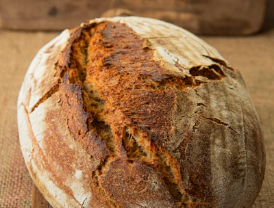 Close-up of a rustic sourdough loaf with a golden crust resting on a wooden board.