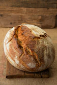 Close-up of a rustic sourdough loaf with a golden crust resting on a wooden board.