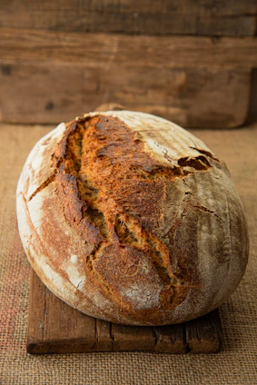 A rustic loaf of golden sourdough bread resting on a wooden board with a dusting of flour.
