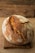 A rustic loaf of bread with a golden-brown crust sits on a wooden board against a burlap background. The bread is oval-shaped with visible scoring on the top, giving it an artisanal appearance.