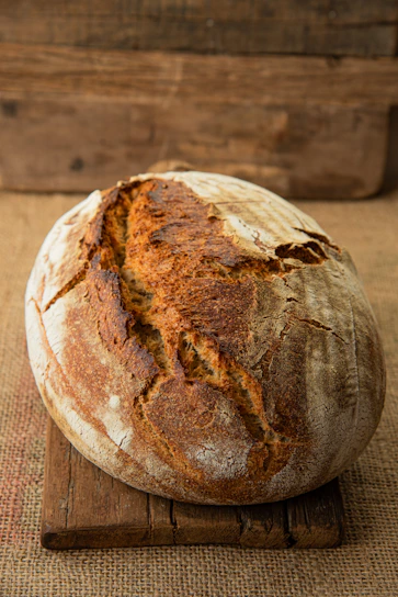 Close-up of a rustic sourdough loaf with a golden crust resting on a wooden board.