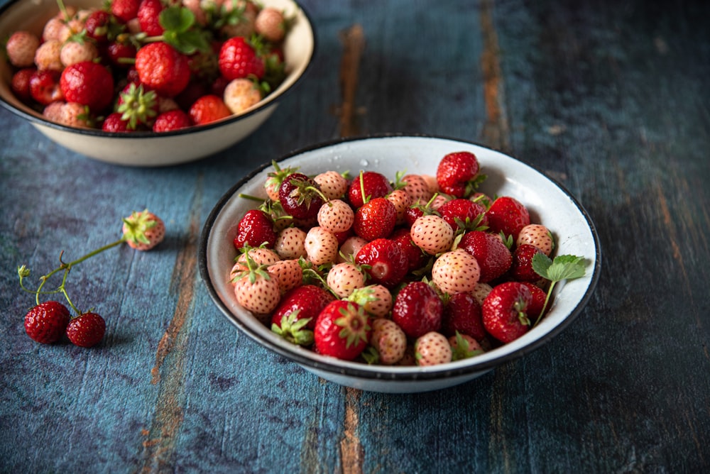 a bowl of strawberries on a table next to a bowl of strawberries