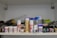 A shelf filled with various art supplies, including spray cans, jars of paint, and bottles of gel. The items are arranged in an organized manner, showcasing a range of brands and types. There are also some metal containers and small tools in the background.