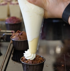 a person is pouring cream on a cupcake