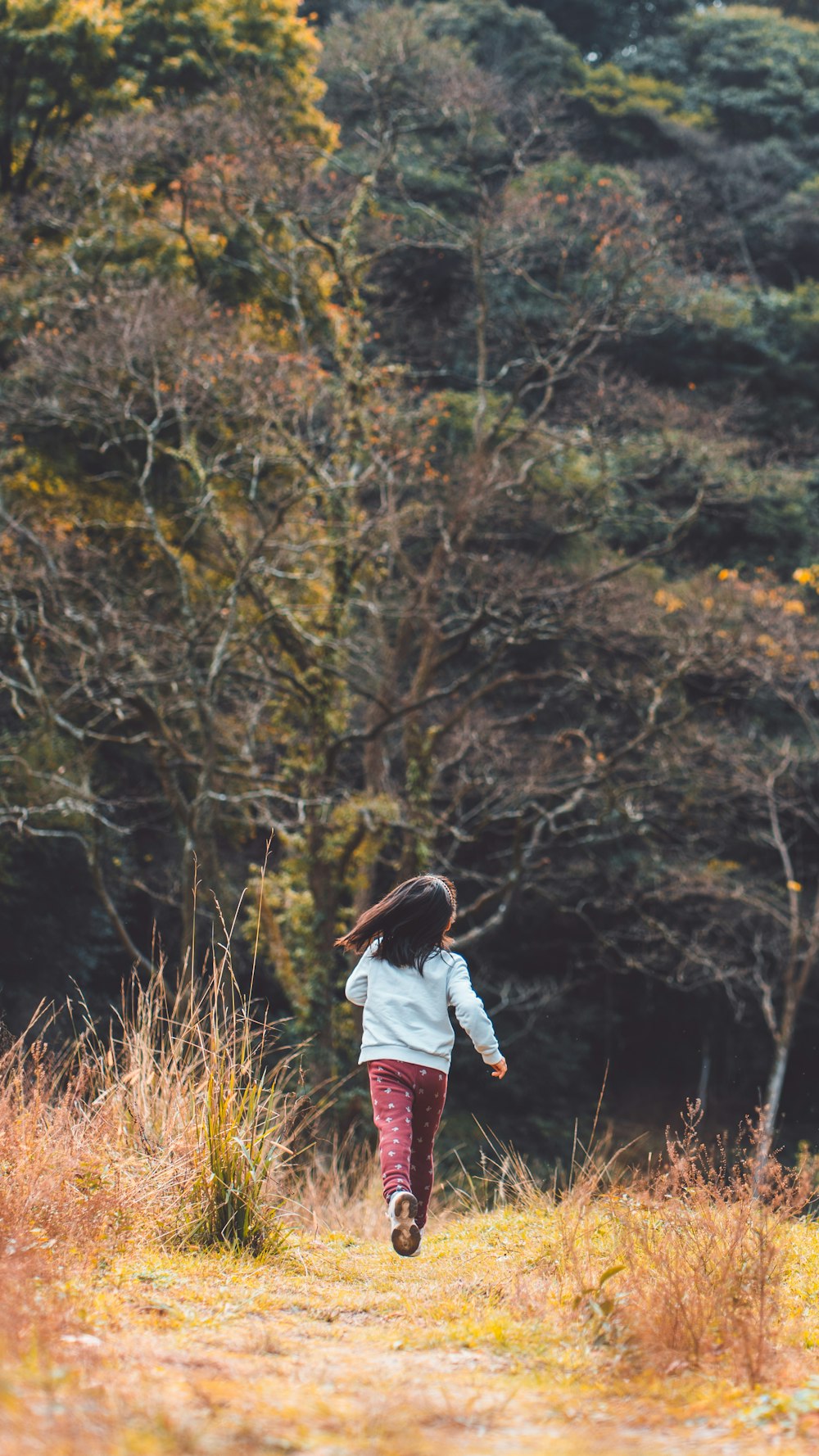 a young girl running through a field with trees in the background