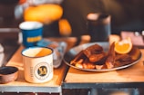 Branded coffee mugs and water bottles arranged on a wooden table with natural light.