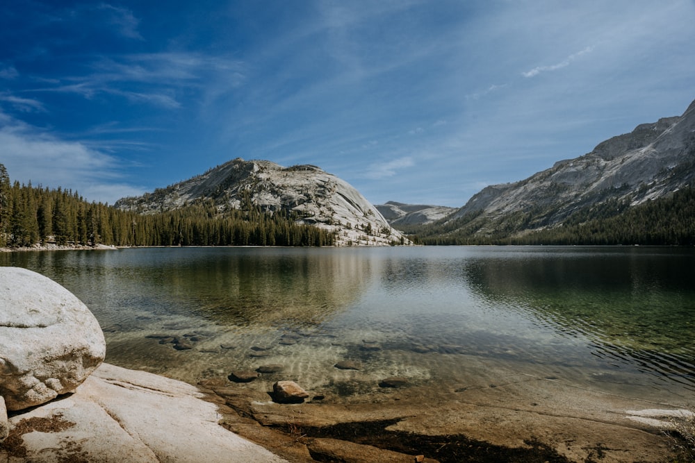 a lake surrounded by mountains and trees under a blue sky