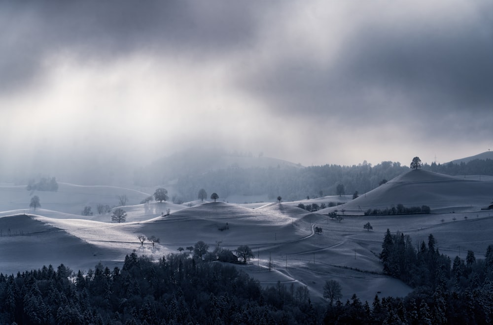 a snowy landscape with trees and hills under a cloudy sky