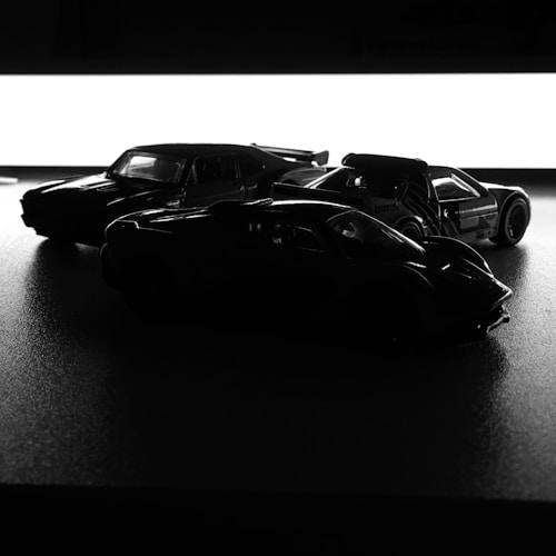 Three model cars are arranged in silhouette against a bright white background, emphasizing their shapes and contours. The lighting creates strong contrasts, highlighting the cars' sleek designs.