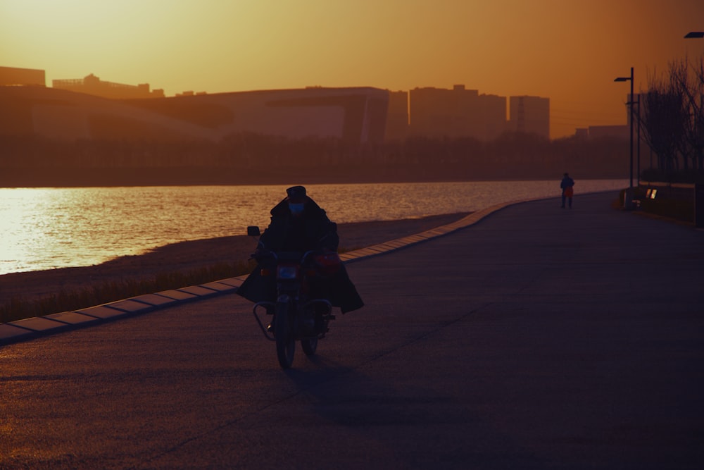 a man riding a motorcycle down a street next to a body of water