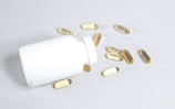 A white plastic bottle lies on its side on a light surface, with several translucent, amber-colored capsules spilling out onto the surface.