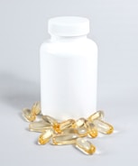 A white plastic bottle with a closed lid is surrounded by several yellowish translucent capsules scattered on a light surface.