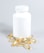 A white plastic bottle with a closed lid is surrounded by several yellowish translucent capsules scattered on a light surface.