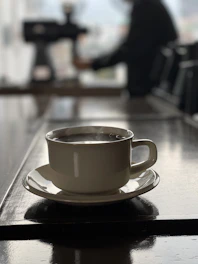 A robotic arm gently serving a steaming cup of coffee on a glass table with neon reflections.