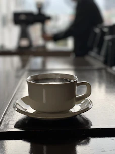 A robotic arm gently serving a steaming cup of coffee on a glass table with neon reflections.