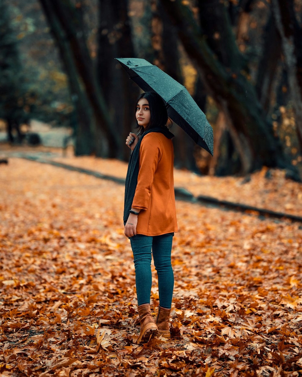 a woman standing in leaves holding an umbrella