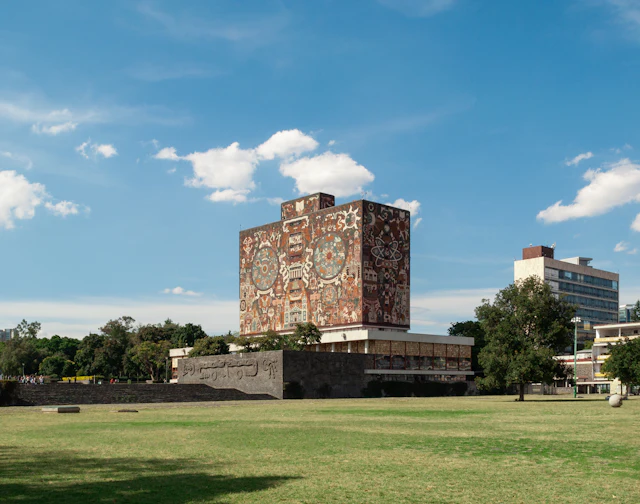 The mosaic-covered Biblioteca Central tower at UNAM's Mexico City campus, seen across the lawn under a blue sky.