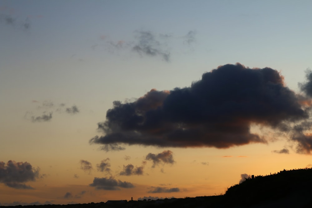 a large cloud is in the sky above a hill