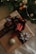 A beautifully wrapped gift with a large red bow is adorned with snowflake-shaped decorations and a gold glittery ornament. The gift is set against a backdrop of lush green fir branches and subtle string lights.