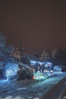 A snowy outdoor scene with a decorated house for the holidays.