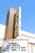 A tall, vintage-style vertical sign with large letters spelling out 'SCAD' is attached to a building. Below the sign, a marquee displays information about the Savannah Music Festival with dates ranging from March 24 to April 9, 2022. The background is a clear blue sky, suggesting a sunny day.
