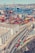 An aerial view of a busy port with numerous colorful shipping containers stacked in rows. Large blue cranes are positioned beside the containers, indicating active loading and unloading operations. In the background, the city skyline with buildings is visible across the water, where additional ships and boats are present. In the foreground, a highway with several trucks transporting containers is shown, adjacent to an industrial building.