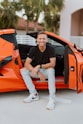 a man sitting in the open door of an orange sports car