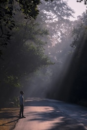 a man standing on the side of a road in the middle of a forest
