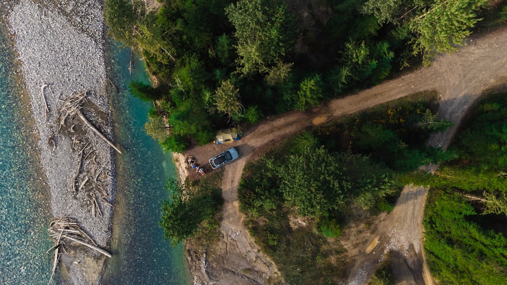 an aerial view of a truck parked on a dirt road next to a body of