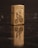 A metallic lighter with a detailed engraving of a cyclist and the word 'Cleveland' is placed upright on a dark reflective surface. The lighter's reflection is visible, creating a mirrored effect.