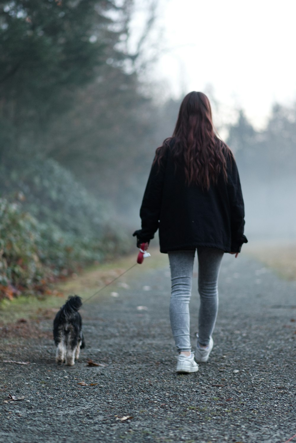 a woman walking a dog down a dirt road