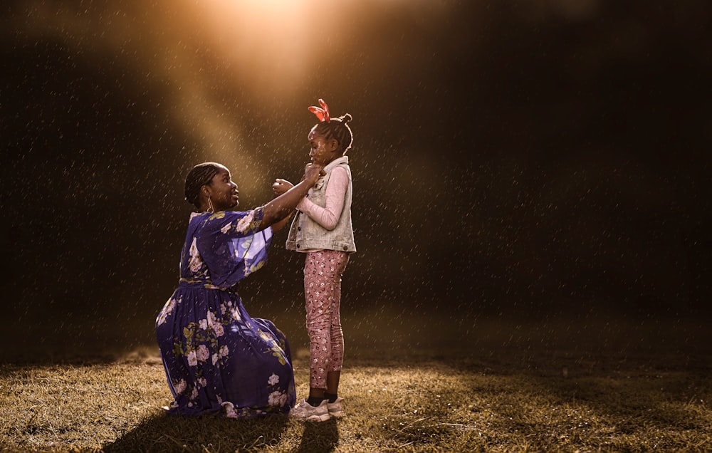 a woman kneeling down next to a little girl