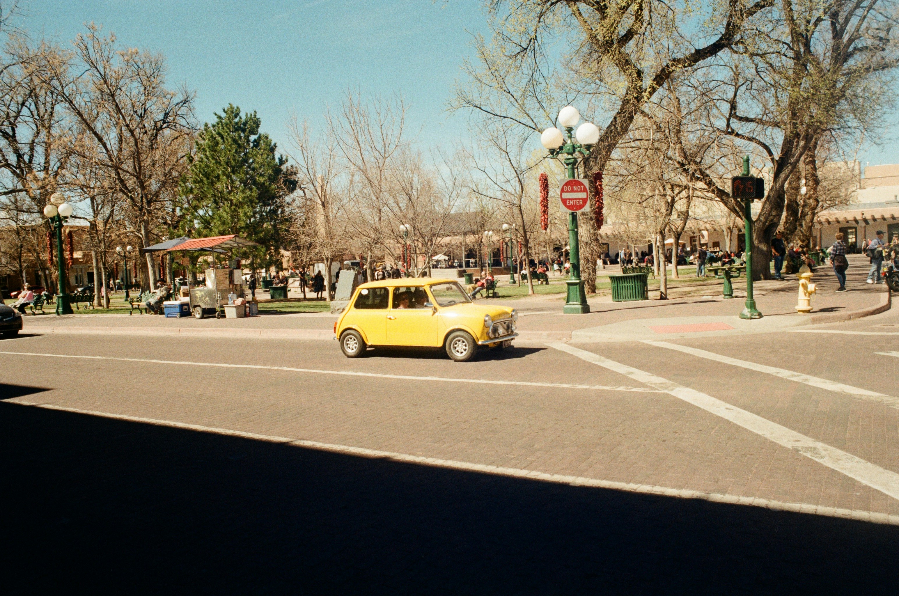a yellow car driving down a street next to a park