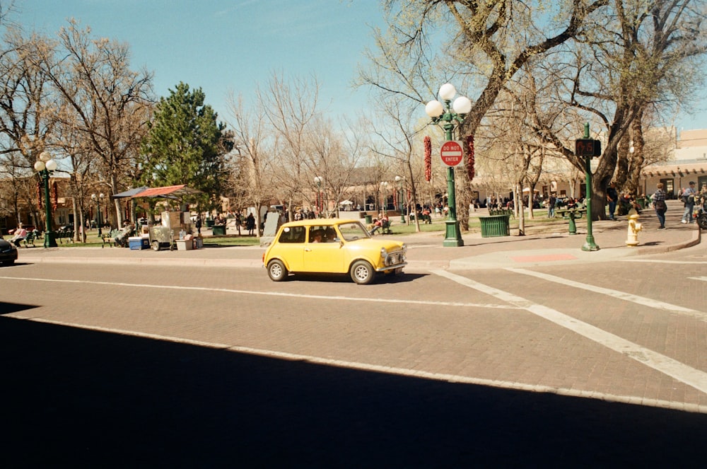 a yellow car driving down a street next to a park