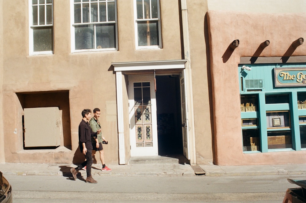 two people walking down the street in front of a building